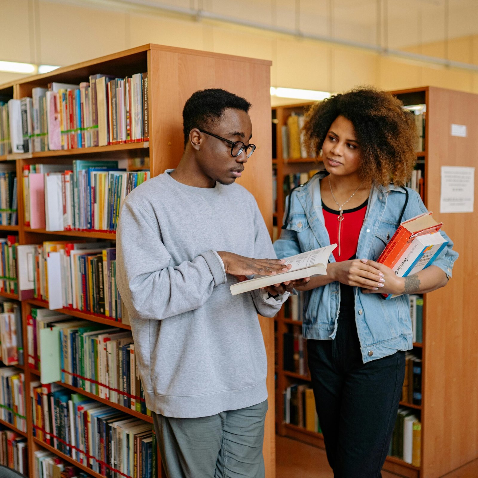 Two students engage in conversation while browsing books in a library.